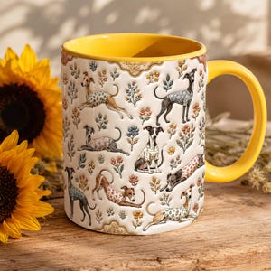 May include: A white ceramic mug with a bright yellow interior and handle, featuring a repeating pattern of greyhound dogs wearing patterned sweaters interspersed with small, colorful floral illustrations across the exterior surface.