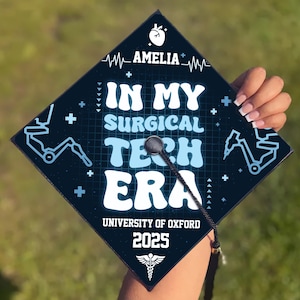 May include: A blue and black graduation cap with the text "In My Surgical Tech Era" and the name "Amelia" on the front. The cap also has a medical symbol and the text "University of Oxford 2025".