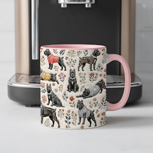 Könnte beinhalten: Ein Keramikbecher mit hellrosa Henkel und Innenseite, verziert mit einem wiederkehrenden Muster aus schwarzen Hunden in verschiedenen Posen und Outfits, durchsetzt mit kleinen bunten Blumenillustrationen auf cremefarbenem Grund.