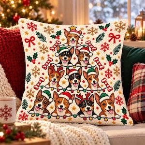 May include: A square throw pillow with a cream-colored background featuring a Christmas tree design composed of nine Basenji dogs wearing Santa hats and reindeer antlers, accented with red bows, green pine sprigs, and candy cane patterns.