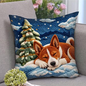 May include: A square throw pillow featuring a textured punch needle design of a brown and white dog sleeping in the snow next to a decorated Christmas tree. The background is a deep blue night sky filled with white stars and fluffy clouds.