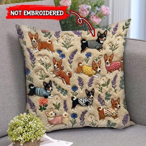 May include: Square beige throw pillow with embroidered Basenji dog designs. The dogs are wearing various outfits and are surrounded by embroidered flowers and foliage. The pillow is on a gray sofa.