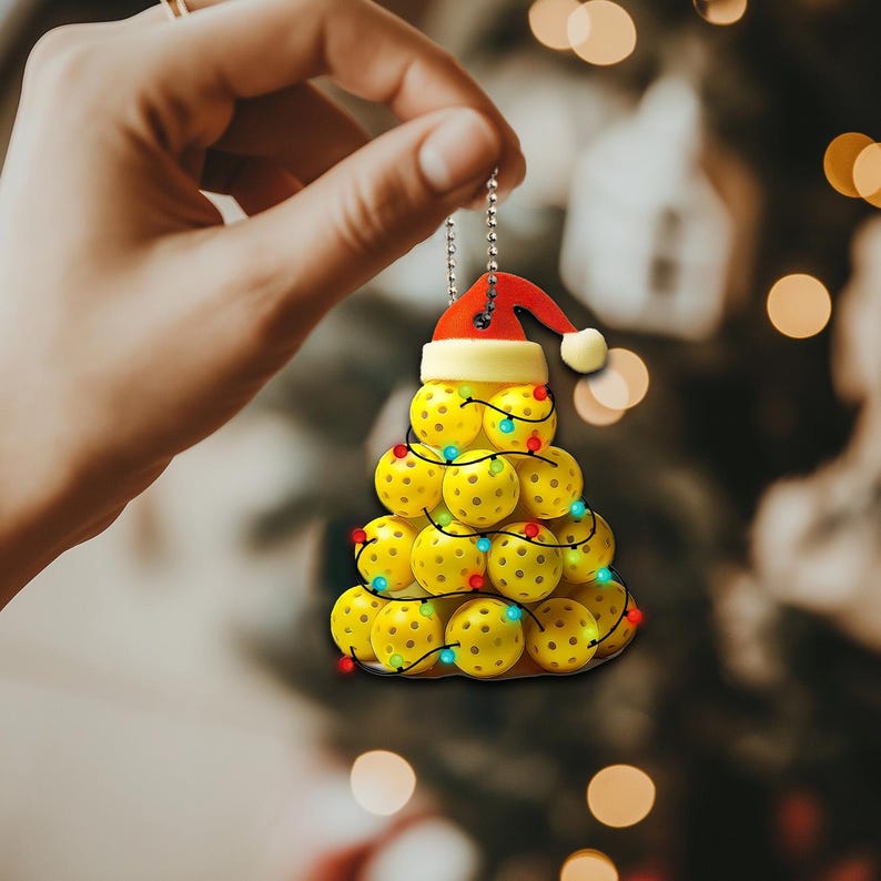 May include: A Christmas tree bauble shaped like a Christmas tree made of yellow pickleball balls with red and green lights. The bauble is topped with a red Santa hat.