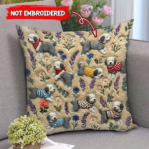 Op de afbeelding: Vierkant kussen met een beige achtergrond, met borduurachtige afbeeldingen van Old English Sheepdogs in verschillende outfits. Het kussen is versierd met bloemen en de tekst "NOT EMBROIDERED".