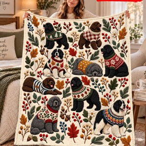 May include: A cream-coloured throw blanket featuring a repeating pattern of Newfoundland dogs wearing various patterned sweaters, interspersed with autumn leaves, berries, pine branches, and acorns. The blanket has a 2D flat printed design.
