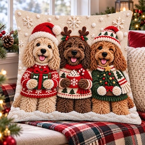 May include: A square throw pillow featuring a textured, three-dimensional embroidered design of three curly-haired dogs wearing holiday sweaters and hats. The dogs are holding a gift, a mug of cocoa, and a small Christmas tree, surrounded by snowflakes.