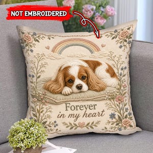 May include: A square throw pillow with a cream background featuring a printed image of a brown and white spaniel dog resting on a cushion. Above the dog is a rainbow and clouds, and below is the text Forever in my heart. The design includes floral borders and small hearts. The text NOT EMBROIDERED is visible at the top.