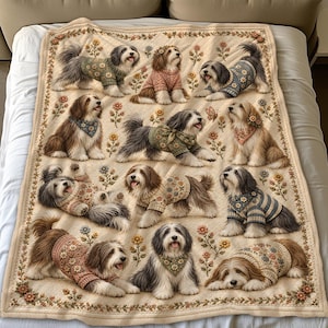 May include: A cream-colored throw blanket featuring a repeating pattern of long-haired dogs in various poses. The dogs are wearing knitted sweaters and bandanas with floral motifs. The blanket is bordered by a delicate floral vine design.