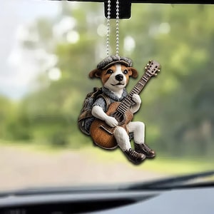 May include: A brown and white dog figurine wearing a blue shirt and a brown hat, playing a brown acoustic guitar. The figurine is hanging from a silver chain.