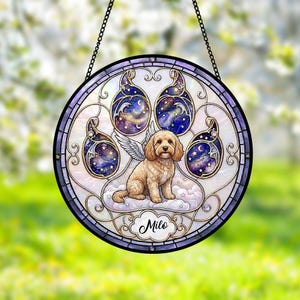 May include: A circular stained glass suncatcher featuring a paw print design with a galaxy-themed background. A light brown dog with angel wings sits in the center on clouds. The name Milo is printed in black script at the bottom of the frame.