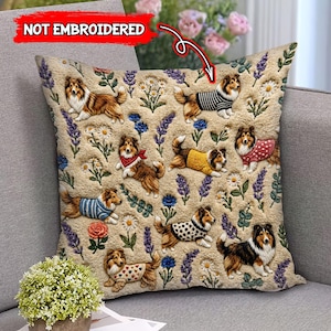 Könnte beinhalten: Beiges quadratisches Kissen mit mehreren Sheltie-Hunde-Illustrationen in verschiedenen Outfits, umgeben von Blumen- und Lavendelmustern. Das Kissen hat eine strukturierte Oberfläche und der Text "NOT EMBROIDERED" ist sichtbar.
