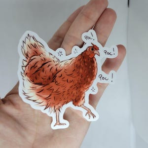 May include: A sticker of a brown chicken with a white chest and a red comb. The chicken is walking and has three speech bubbles that say "Roc!" in black text.