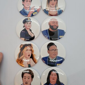 May include: Eight round button badges featuring cartoon illustrations of people wearing blue shirts with name tags. The name tags include the names "Jared", "Greg", "Mateo", "Cloud", and "Glen".