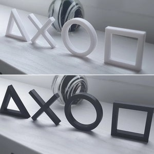 May include: Two sets of white and black geometric shapes, including a triangle, an X, a circle, and a square. The shapes are arranged in a row on a white surface.