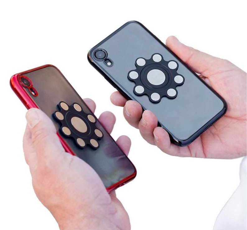 May include: Two black mobile phone cases with a black and silver magnetic phone ring holder attached to the back of each case.