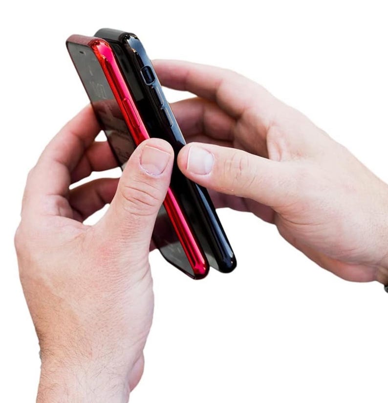 May include: Two smartphone cases side-by-side, one black and one red. The cases are held in a person's hands.