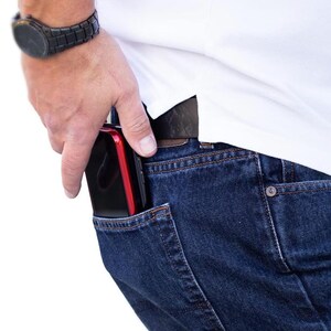 May include: A person wearing blue jeans with a black and red phone in the back pocket.