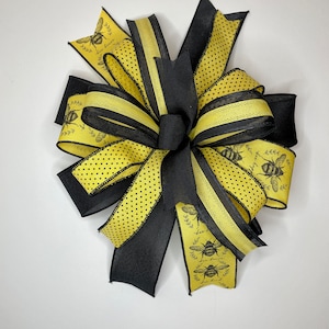 May include: A yellow and black bow with a bee and floral print. The bow is made of ribbon with black polka dots and a black satin ribbon.