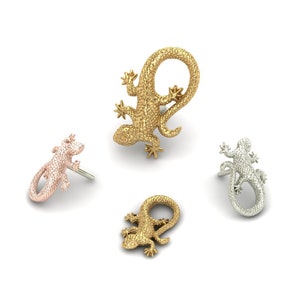 May include: Four gold-toned lizard-shaped earrings. Two are larger and two are smaller. The larger earrings are curled into a circle shape. The smaller earrings are straight.