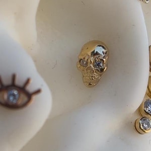 May include: Gold skull earring with clear cubic zirconia stones for the eyes.