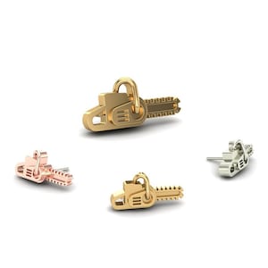 May include: Three gold-coloured earrings shaped like chainsaws. The earrings are in different sizes and are on a white background.