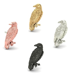 Puede incluir: Cuatro figuras de cuervo en diferentes acabados metálicos: oro rosa, oro, plata y negro. Cada cuervo está posado, mostrando texturas detalladas de plumas y un pico realista. Las aves se exhiben sobre un fondo blanco.