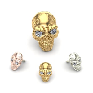 May include: Three skull earrings with diamond eyes. The earrings are in gold, rose gold, and silver.