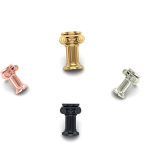 May include: Four miniature Ionic columns in various metallic finishes: gold, silver, rose gold, and black. Each column has a detailed capital and fluted shaft, set against a white background. These decorative items are likely used for jewellery or miniature displays.