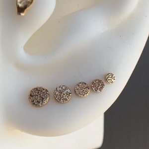 May include: Four gold-toned textured round earrings of different sizes, displayed on a white mannequin ear.