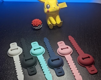 May include: A collection of six silicone cable organizers in white, black, teal, navy, pink, and burgundy. A paper Pikachu figure and a pixelated Pokeball are in the background.