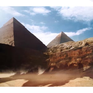 May include: A scenic view of the Giza pyramids in Egypt under a partly cloudy blue sky. The pyramids are brown and tan, with a sandy foreground and a hint of wind-blown dust. The image captures the grandeur of ancient architecture.