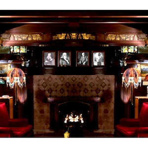 May include: A cozy, dark-wood paneled room with a fireplace, framed portraits, and ornate lamps. The fireplace has a decorative tile surround, and the room features red velvet armchairs, creating a warm and inviting atmosphere.