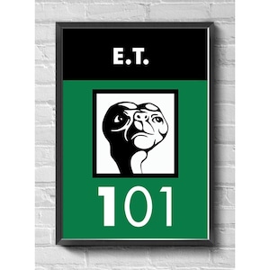 Pode incluir: Pôster emoldurado com o texto "E.T." acima de um retângulo verde com o número "101" em branco. O retângulo verde contém uma imagem em preto e branco do personagem E.T. A moldura é preta.