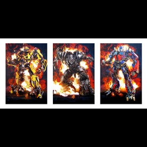 Op de afbeelding: Een drieluik van actievolle afbeeldingen met Transformers-personages. Het kunstwerk toont Bumblebee in geel, Megatron in zilver en Optimus Prime in rood en blauw, allemaal tegen een vurige achtergrond. De afbeeldingen zijn wit omlijst.