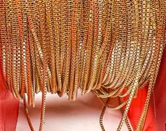 May include: A spool of gold-colored chain, wound tightly around a red spool. The chain is made of small, square links.