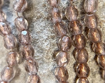 May include: Close-up of several strands of faceted, translucent beads in shades of mauve and brown. The beads are strung together, creating a textured and layered effect. The background is a rough, gray stone surface.