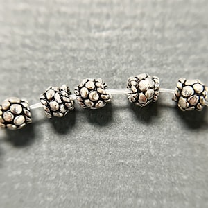 May include: A strand of silver beads with a textured, hammered finish. Each bead has a slightly rounded shape and is connected to the next bead with a clear elastic string.
