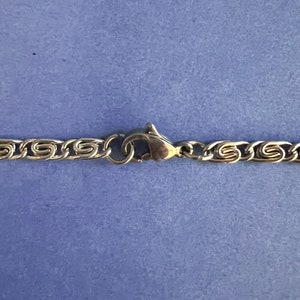 May include: Close-up of a silver chain necklace with a lobster clasp closure.