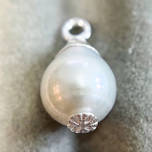 May include: A white pearl charm with a silver loop and a silver decorative detail at the bottom.
