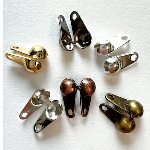 May include: Assortment of six metal clasps with ball ends. The clasps are in various finishes, including silver, gold, and bronze.