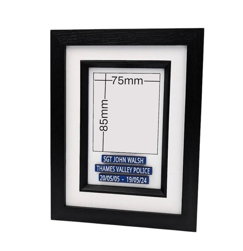 May include: A black framed picture with a white mat. The frame holds a white rectangle with the dimensions 85mm x 75mm. Below the rectangle are three blue lines of text that read: "SGT JOHN WALSH", "THAMES VALLEY POLICE", and "20/05/05 - 19/05/24".