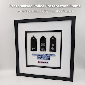 May include: A black framed presentation featuring three police epaulettes. The epaulettes are black with silver insignia. A blue nameplate reads "DETECTIVE INSPECTOR SARAH NORTON-SHAW" and "THAMES VALLEY POLICE".