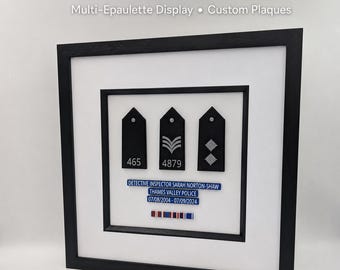 May include: A black framed presentation featuring three police epaulettes. The epaulettes are black with silver insignia. A blue nameplate reads "DETECTIVE INSPECTOR SARAH NORTON-SHAW" and "THAMES VALLEY POLICE".
