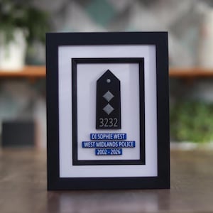 May include: Framed black plaque featuring a police badge with the number 3232 and the name DI Sophie West. The text "WEST MIDLANDS POLICE 2002-2026" is also displayed. The plaque is set against a white background within a black frame.