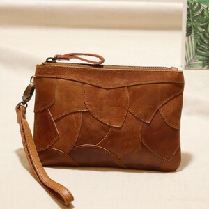 May include: A brown leather clutch with a zip fastening and a detachable strap. The clutch features a unique patchwork design with different sized pieces of leather stitched together.