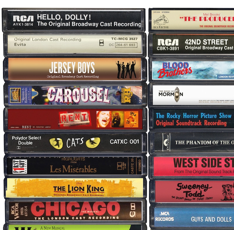 May include: A collection of vintage cassette tapes featuring Broadway show soundtracks. The tapes are arranged vertically in two columns. The titles include "Hello, Dolly!", "Evita", "Jersey Boys", "Carousel", "Rent", "Cats", "Les Mis&eacute;rables", "The Lion King", "Chicago", "The Producers", "42nd Street", "Blood Brothers", "The Book of Mormon", "The Rocky Horror Picture Show", "The Phantom of the Opera", "West Side Story", "Sweeney Todd", and "Guys and Dolls".