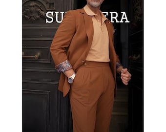 Pode incluir: Um fato castanho com uma camisa polo a condizer. O fato apresenta um blazer de dois botões e calças com pregas. A camisa polo é num tom mais claro de castanho. Os punhos do blazer têm um forro estampado. Um relógio branco é visível. As palavras "SU" e "FRA" são visíveis.