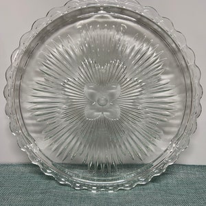 May include: A clear glass cake stand with a scalloped edge and a starburst design in the centre.