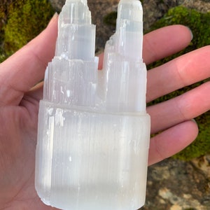 May include: White selenite crystal tower with a unique, naturally formed double peak. The crystal is smooth and polished, with a white, translucent appearance.