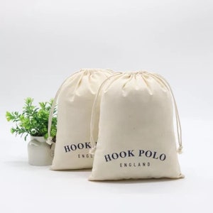 May include: Two off-white cotton drawstring bags with navy blue text. The text on the bag on the right reads "HOOK POLO ENGLAND". The text on the bag on the left reads "HOOK ENGLAND".